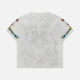 The Cindy Embroidered Cropped T-shirt by ALICE + OLIVIA is shown laid flat with the back facing up, highlighting its colorful floral embroidery along the edges of both sleeves. This chic white tee features a playful, delicate floral design that adds a vibrant touch to any outfit.