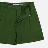 Introducing the Conry Relaxed Long Pleated Short by ALICE + OLIVIA: these dark green linen shorts feature a relaxed fit with front pleats, side pockets, and an open zipper fly. The waistband is finished with a hook-and-bar closure, and the inside tag displays the ALICE + OLIVIA brand name. The shorts are shown on a white background.