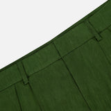 Close-up of the waistband and pleats of the Conry Relaxed Long Pleated Short by ALICE + OLIVIA in dark green, featuring belt loops and linen fabric texture against a white background. The image showcases the relaxed fit and classic detailing that define these pleated shorts.