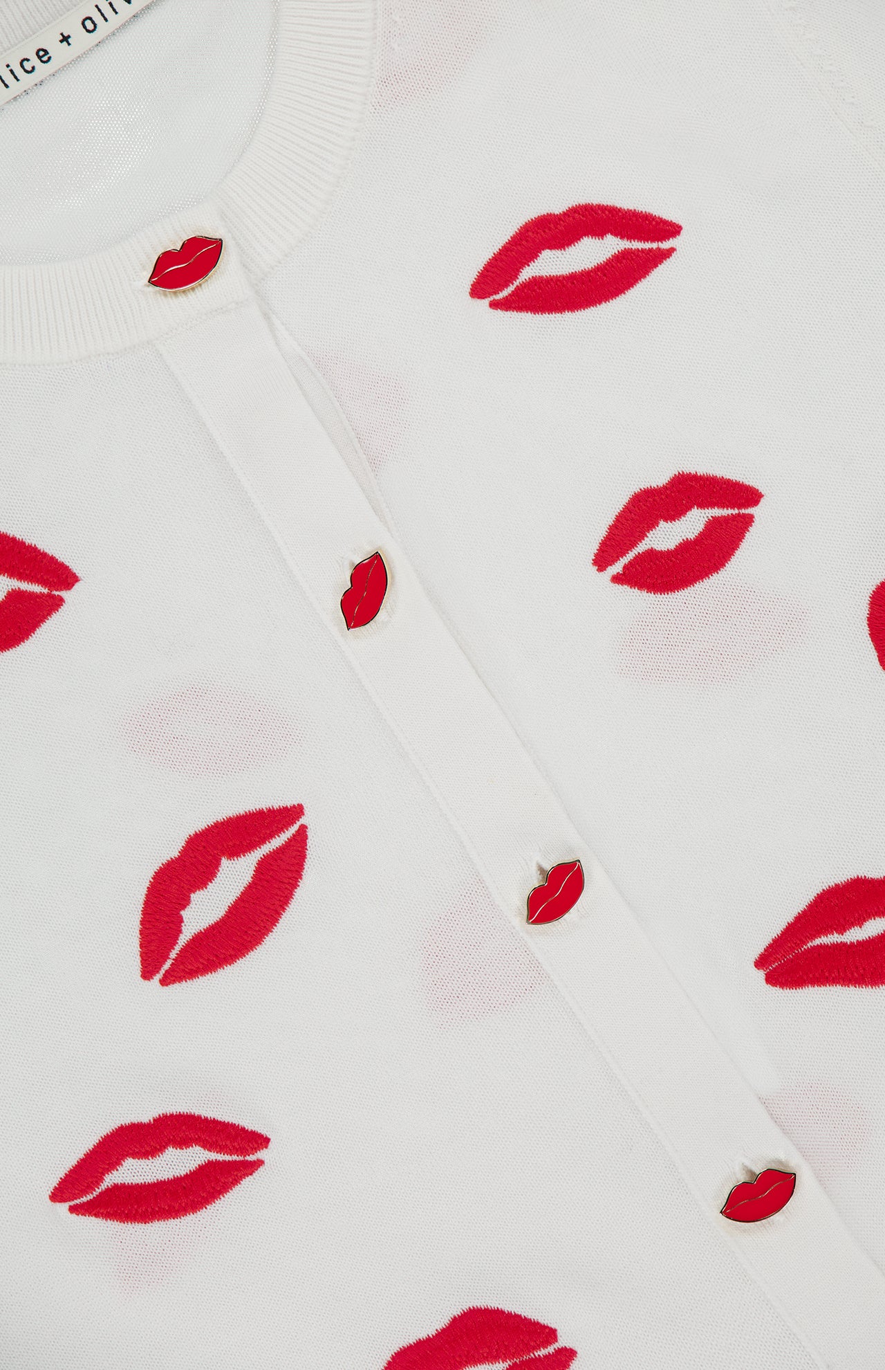 The Daroda Lip Cardigan Sweater by ALICE + OLIVIA is a cropped white knit with embroidered lips prints and red lips-shaped buttons on the front.