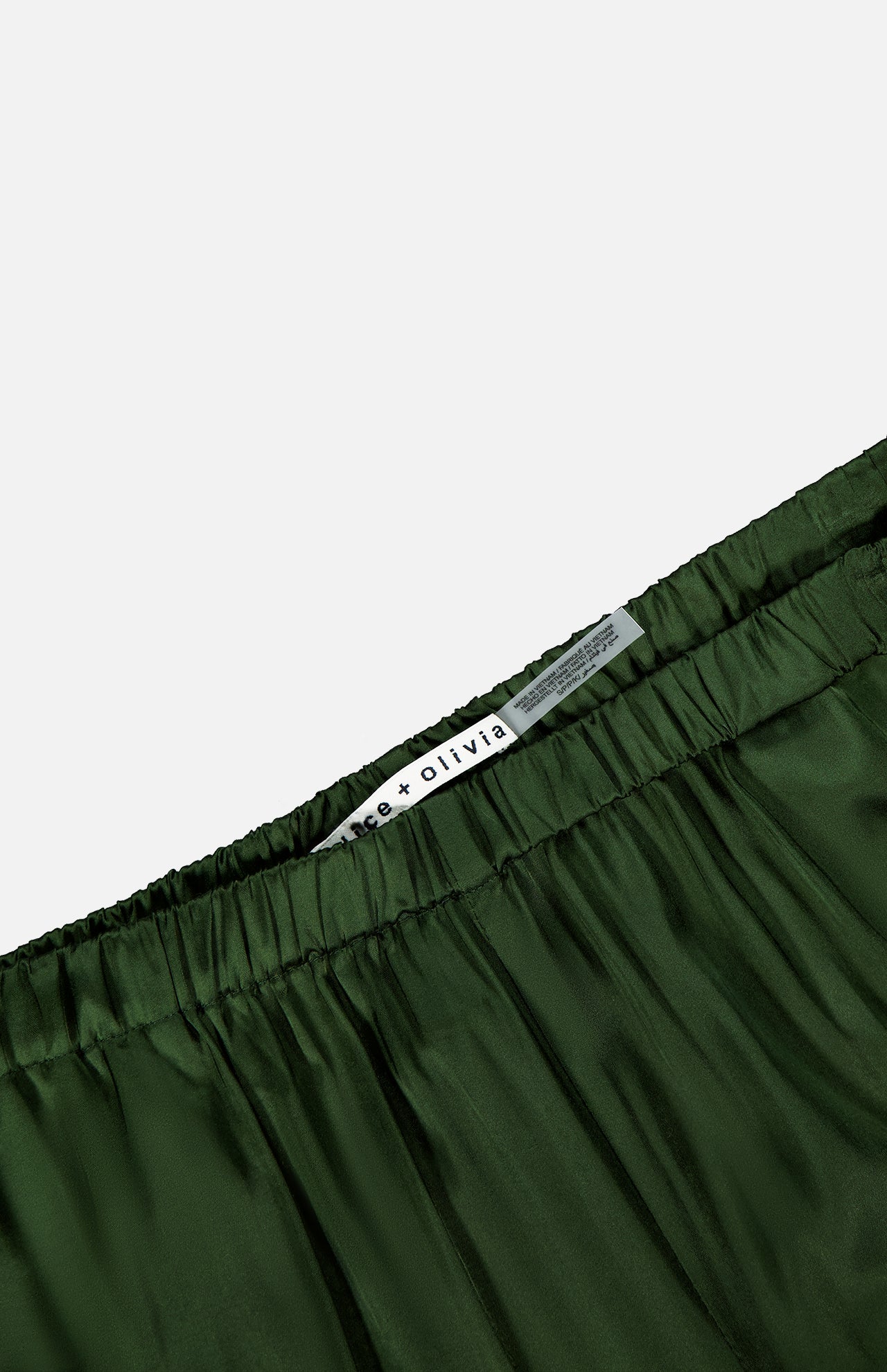 Close-up of the waistband of dark green, silky Declan Pull On Genie Pant by ALICE + OLIVIA, featuring a white label with the brand name against a plain background.