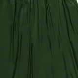 Close-up of the Declan Pull On Genie Pant in dark green silky charmeuse, featuring an elastic waistband and a visible ALICE + OLIVIA label at the top. The shiny fabric has a slightly pleated appearance.