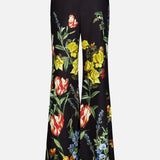 The photo shows the back view of the Dylan High Rise Wide Leg Pant by ALICE + OLIVIA—black, high-waisted linen trousers featuring a vibrant dark floral pattern with red, yellow, and blue flowers, green leaves, and a light-colored hem at the bottom.