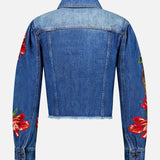 The Elijah Embellished Applique Cropped Denim Jacket by ALICE + OLIVIA is displayed from the back against a plain white background, showcasing its blue denim construction, cropped silhouette with a raw hem, and long sleeves adorned with red embroidered floral appliques.
