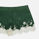 The Elissa Cutaway Lace Short by ALICE + OLIVIA features dark green satin with a smooth, shiny finish, detailed with white lace trim and delicate embroidered florals along the hem—offering a chic summer-in-the-Hamptons vibe.