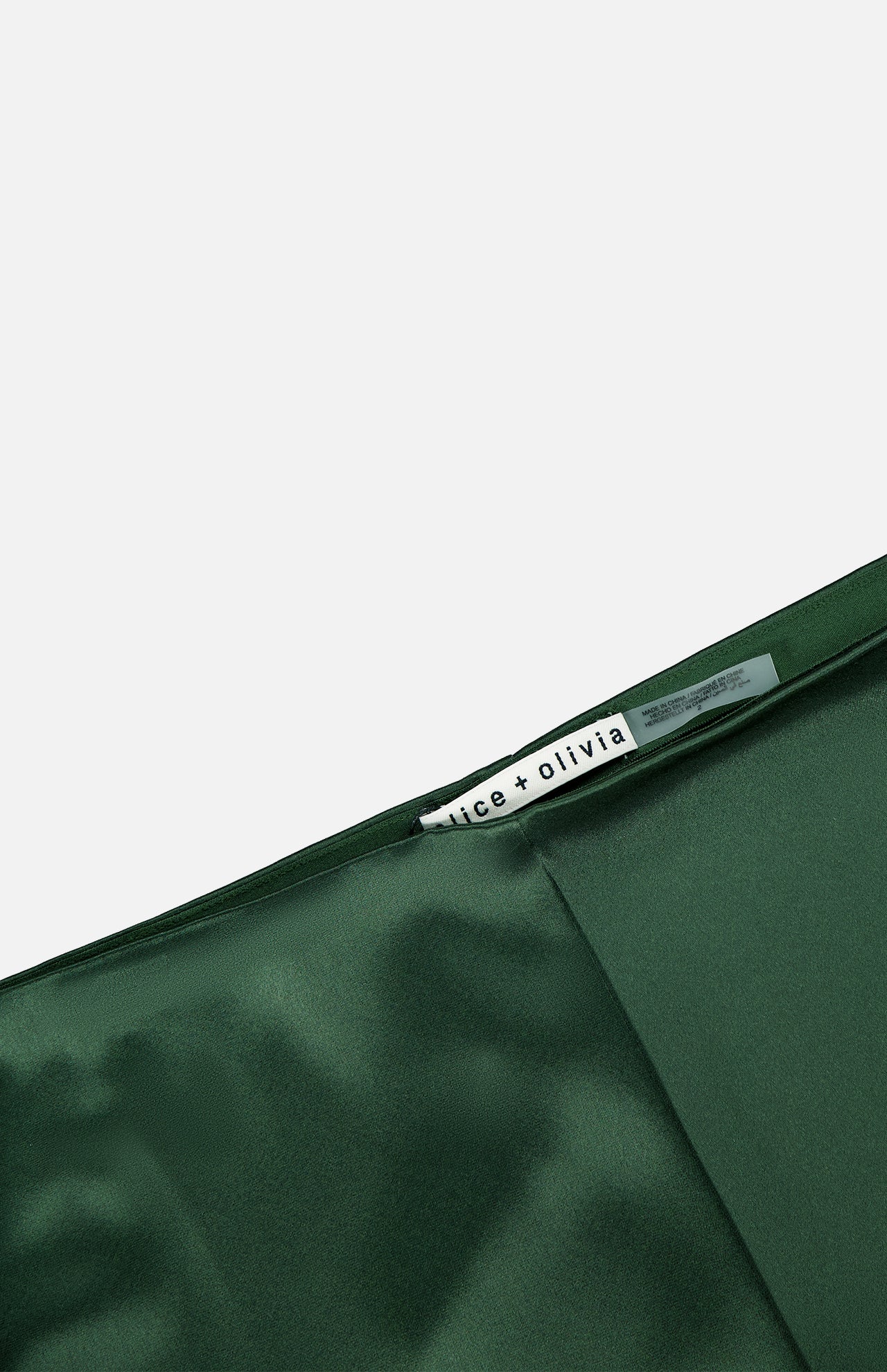 A close-up of the Elissa Cutaway Lace Short by ALICE + OLIVIA reveals its lustrous dark green satin fabric and delicate lace trim, with the brand label visible on the inside seam. Set against a plain background, the image exudes effortless summer-in-the-Hamptons elegance.