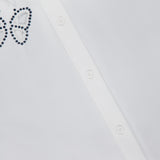 Close-up of the ALICE + OLIVIA Finely Embellished Button Down with Cutouts, a white blouse adorned with butterfly-shaped patterns outlined in small dark beads or studs, and featuring delicate cut-out details for an extra touch of elegance.