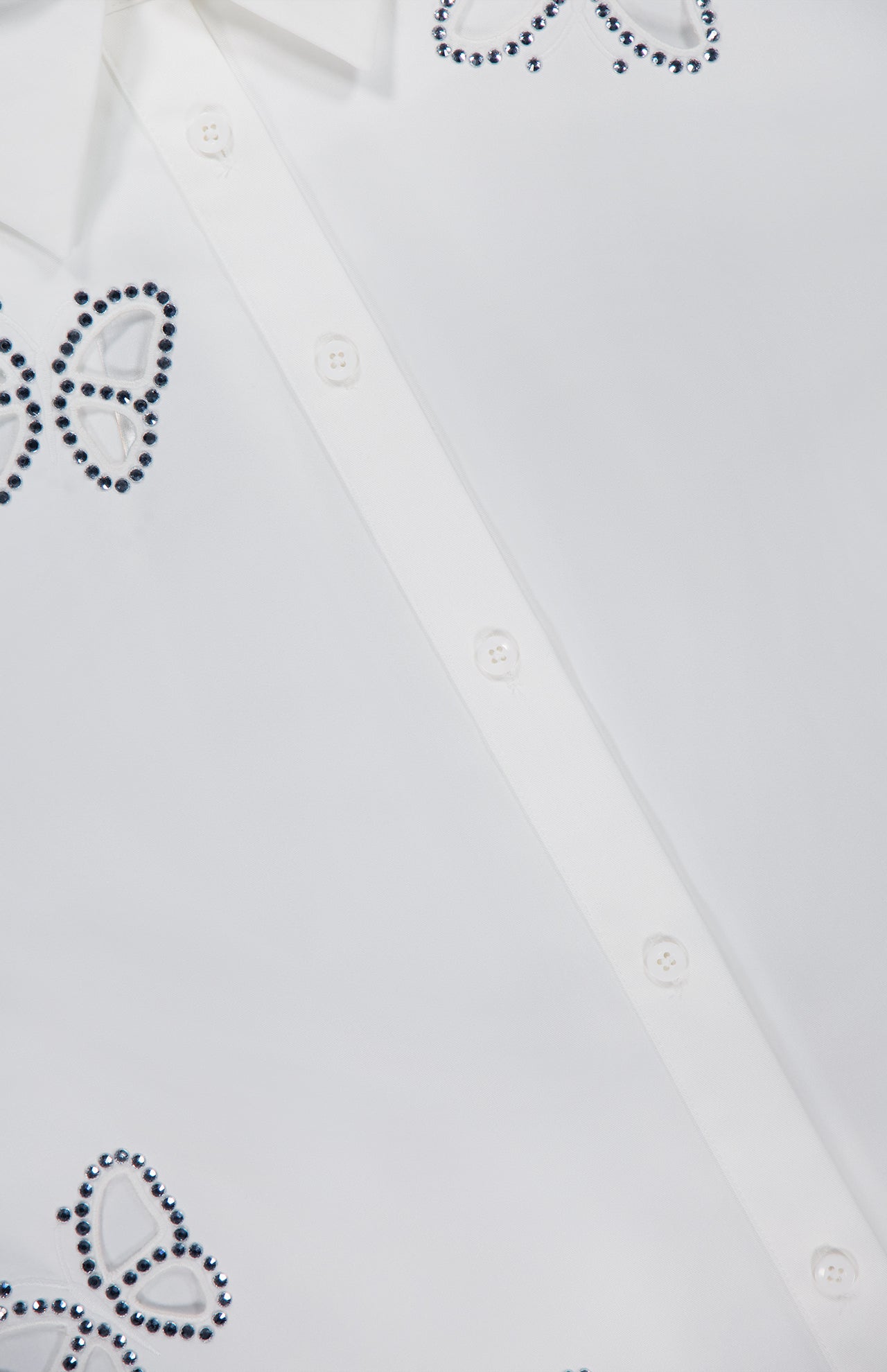 Close-up of the ALICE + OLIVIA Finely Embellished Button Down with Cutouts, a white blouse adorned with butterfly-shaped patterns outlined in small dark beads or studs, and featuring delicate cut-out details for an extra touch of elegance.