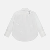 The ALICE + OLIVIA Finely Embellished Button Down with Cutouts is shown from the back, highlighting its delicate butterfly-shaped cut-out patterns and a small embroidered butterfly near the shoulder. These elegant details lend an air of sophistication to this classic white long-sleeve blouse.