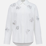 The Finely Embellished Button Down with Cutouts by ALICE + OLIVIA is a sophisticated white long-sleeve blouse with a classic collar and button-up front, featuring scattered butterfly outlines crafted from small black and silver studs across the front, sleeves, and upper chest. Delicate crystal embellishments add an elevated touch of sparkle to this elegant design.