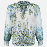 The ALICE + OLIVIA Ilan Pleated Blouson Sleeve Button Front Blouse features a white base with blue and green floral print, pleated sleeves, patterned cuff trim, V-neckline, and relaxed fit for effortless elegance.