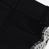 Close-up of the Olivia Pant with Cutaway Lace Godet by ALICE + OLIVIA, featuring a black waistband, belt loops, back pocket, and cutwork lace trim along the side.