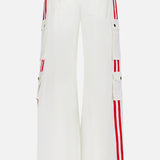 The image shows the Olympia Mr Baggy Cargo Pant With Side Stripe by ALICE + OLIVIA, featuring a white wide-leg design, red vertical side stripes, cargo pockets with button flaps, and a red, white, and blue striped waistband.