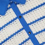 Close-up of a textured, cream knit fabric with horizontal blue stripes, a blue collar, blue button placket, and silver buttons. The Randall Pointelle Polo Cardigan by ALICE + OLIVIA is a lightweight summer knitwear piece featuring subtle pointelle details for a breezy finish.