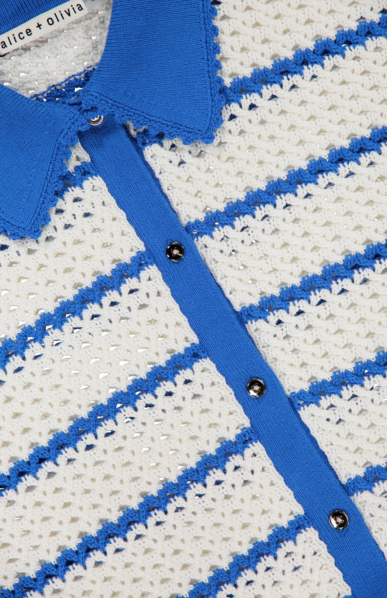 Close-up of a textured, cream knit fabric with horizontal blue stripes, a blue collar, blue button placket, and silver buttons. The Randall Pointelle Polo Cardigan by ALICE + OLIVIA is a lightweight summer knitwear piece featuring subtle pointelle details for a breezy finish.