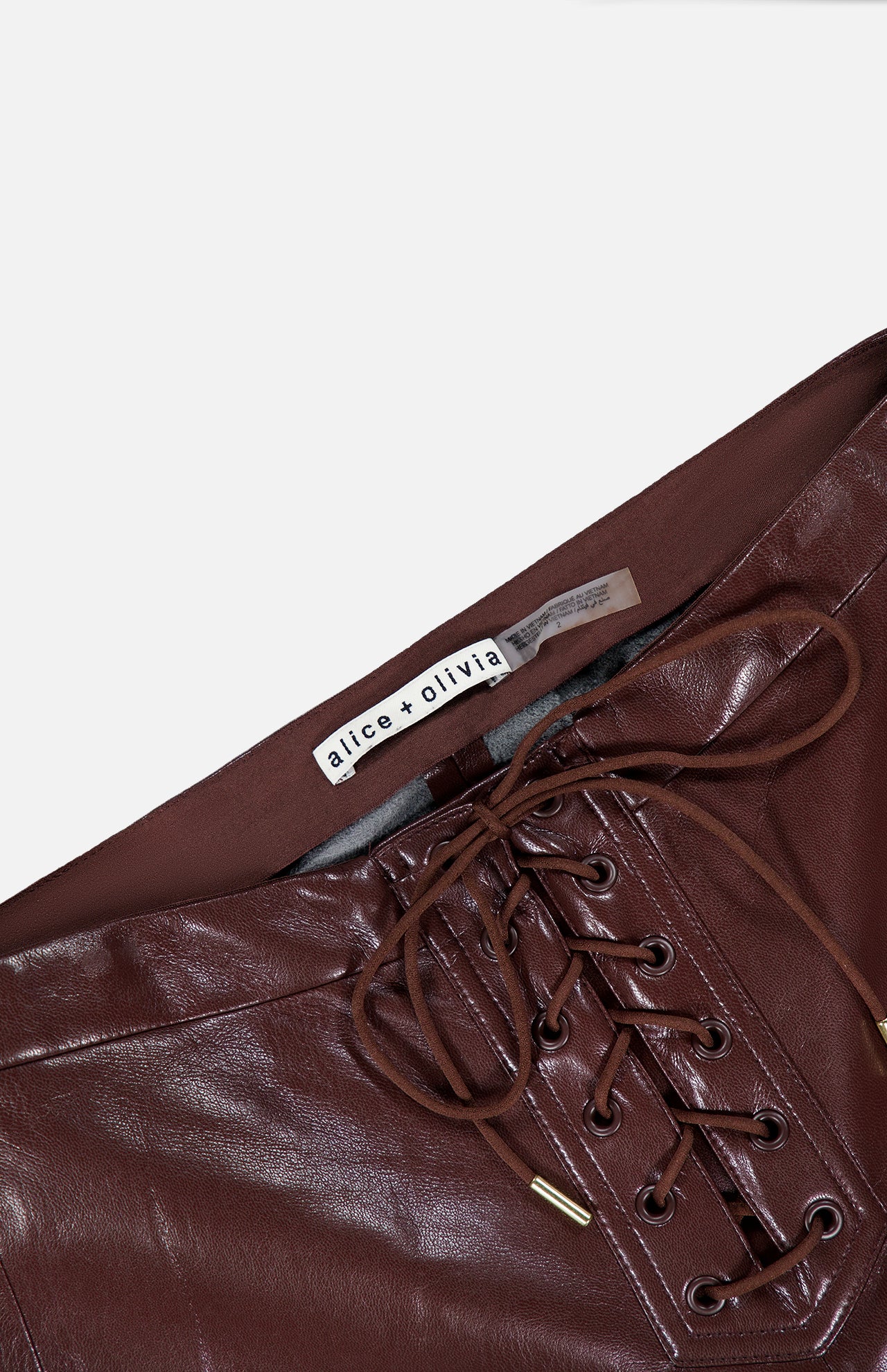 Close-up of the brown Ravyn Vegan Leather Lace Up Bootcut Pant by ALICE + OLIVIA, featuring a low-rise fit, lace-up front, and a visible ALICE + OLIVIA label on the waistband.