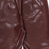 A close-up of the ALICE + OLIVIA Ravyn Vegan Leather Lace Up Bootcut Pant in shiny maroon, featuring low-rise styling and pleats at the waist to highlight the rich texture and vegan leather material.
