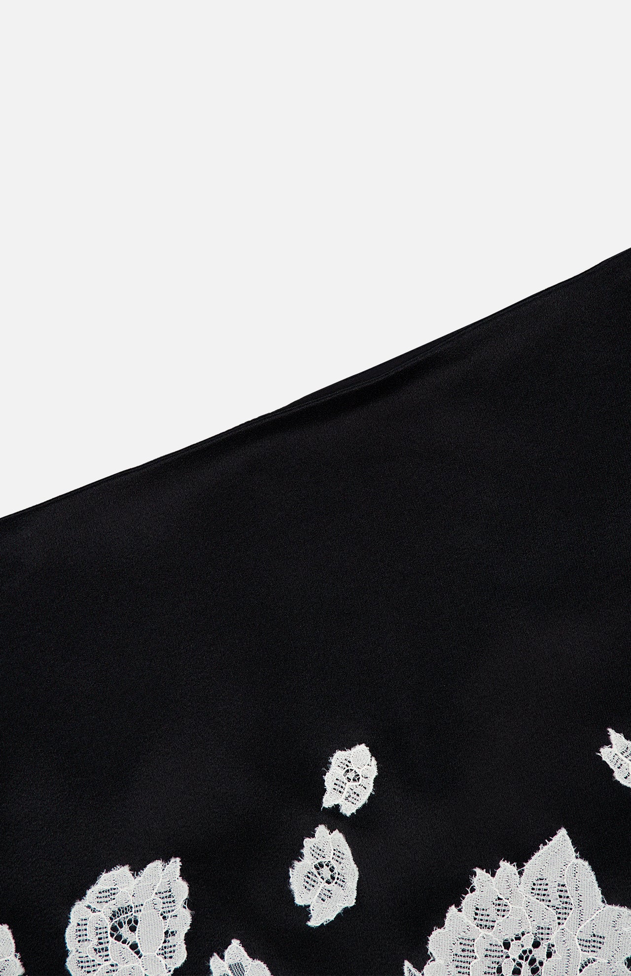 A close-up of the Rubi Lace Trim Low Rise Micro Skirt by ALICE + OLIVIA, featuring black fabric and white floral cutwork lace trim at the hem, set against a plain light background.