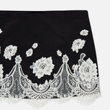 The Rubi Lace Trim Low Rise Micro Skirt by ALICE + OLIVIA features white floral lace embroidery, scalloped edges, and intricate cutwork trim on a solid black low-rise micro silhouette.