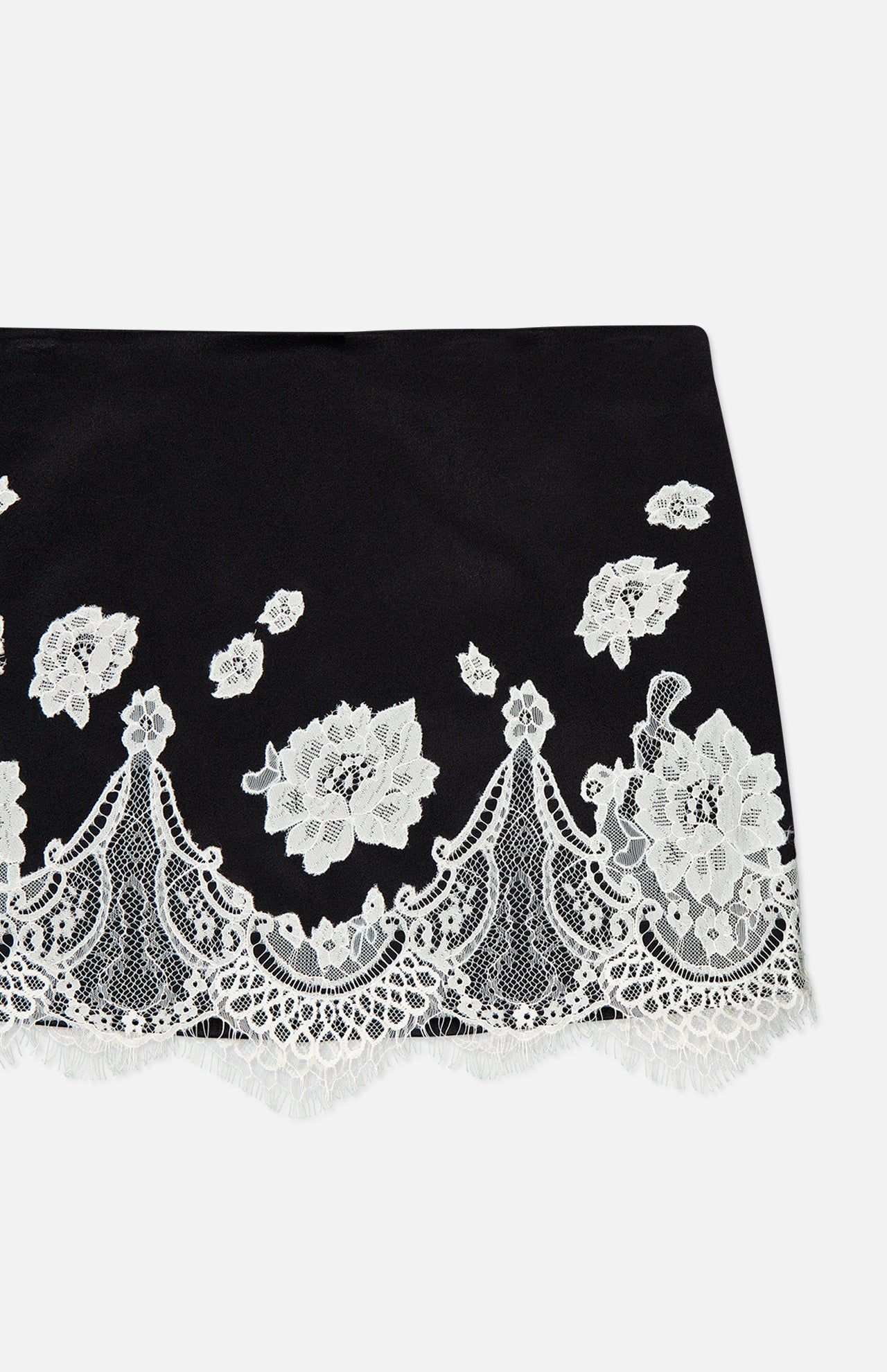 The Rubi Lace Trim Low Rise Micro Skirt by ALICE + OLIVIA features white floral lace embroidery, scalloped edges, and intricate cutwork trim on a solid black low-rise micro silhouette.