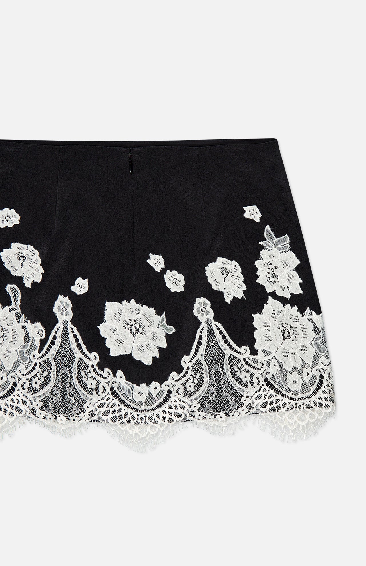 The Rubi Lace Trim Low Rise Micro Skirt by ALICE + OLIVIA features black fabric with white floral lace embroidery, cutwork lace trim, and a scalloped lace hem, shown on a plain white background.