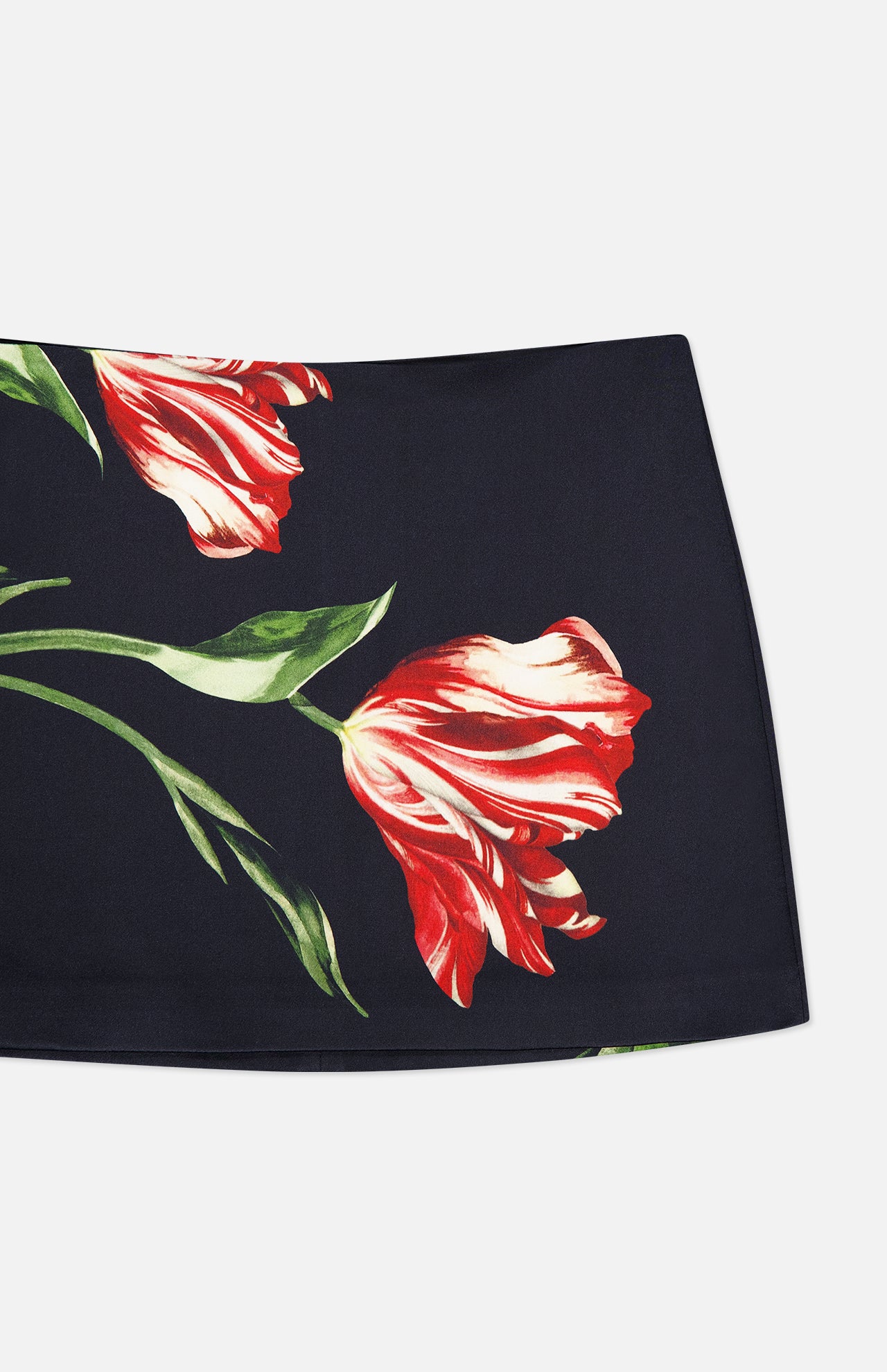 The Rubi Low Rise Floral Skirt by ALICE + OLIVIA is a black mini skirt adorned with a large red and white flower, complete with green stems and leaves printed on the fabric.