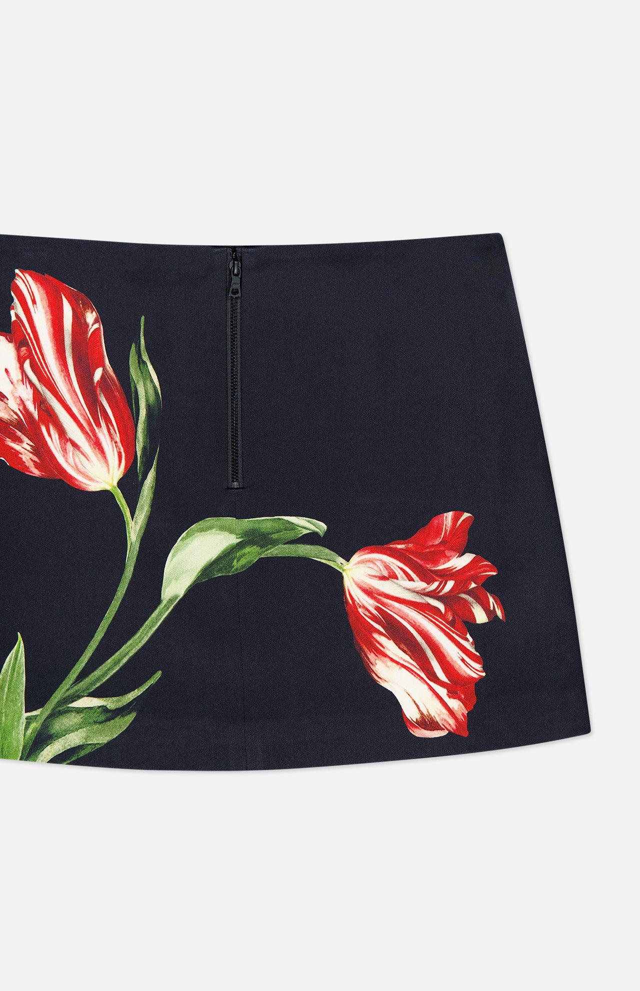 The Rubi Low Rise Floral Skirt by ALICE + OLIVIA features a navy mini silhouette with a black zipper and a striking red and white tulip flower print, accented by green leaves on the front.