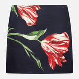 The ALICE + OLIVIA Rubi Low Rise Floral Skirt showcases a striking large red and white tulip print with vivid green leaves on a black mini silhouette, displayed flat against a white background—an ideal piece to bring romantic flair to your wardrobe.