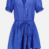 The Thalia Puff Sleeve Tunic Dress by ALICE + OLIVIA is a bright cobalt blue, short-sleeved dress featuring buttons down the front, a tied waist belt with tassels, and an embroidered flared skirt. Crafted from lightweight, slightly textured eyelet cotton voile, this tunic blends effortless style with breezy bohemian flair.