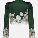 The Thomasina Puff Sleeve Cropped Jacket by ALICE + OLIVIA is a dark green satin piece with stylish puff sleeves, featuring delicate white bloom cutwork lace florals across the back and cuffs, and finished with a scalloped lace hem, shown against a plain white background.