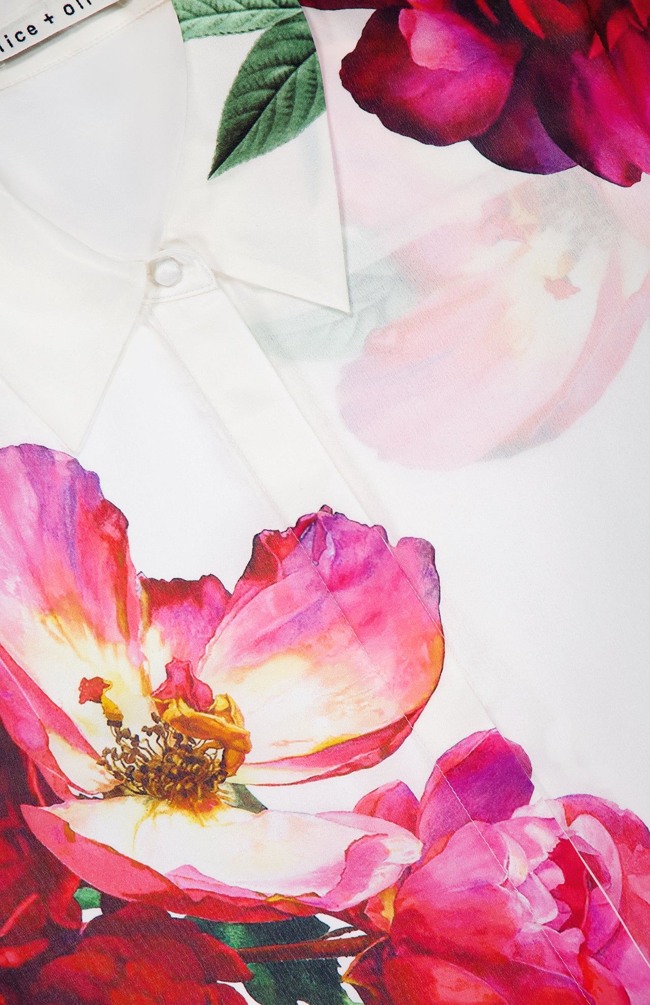 Close-up of the ALICE + OLIVIA Willa Hidden Placket Silk Top, a white blouse with bright pink and red floral prints and green leaves—ideal for adding a designer touch to your outfit.