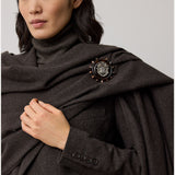 Dressed in a dark turtleneck and the Mini Herringbone Blazer from RALPH LAUREN COLLECTION, accented with a decorative brooch featuring a detailed central emblem and delicate round embellishments, this ensemble exudes refined elegance.