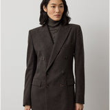 A person with shoulder-length dark hair wears the RALPH LAUREN COLLECTION Mini Herringbone Blazer, featuring a double-breasted design in dark brown wool, styled over a matching turtleneck sweater and standing against a plain light background.
