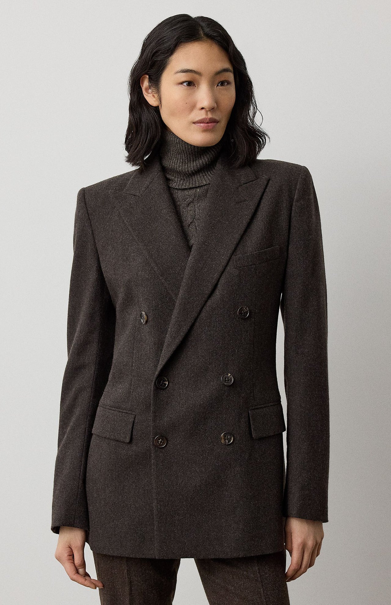 A woman wearing a dark brown Mini Herringbone Blazer by Ralph Lauren Collection over a matching turtleneck sweater with a detachable scarf.