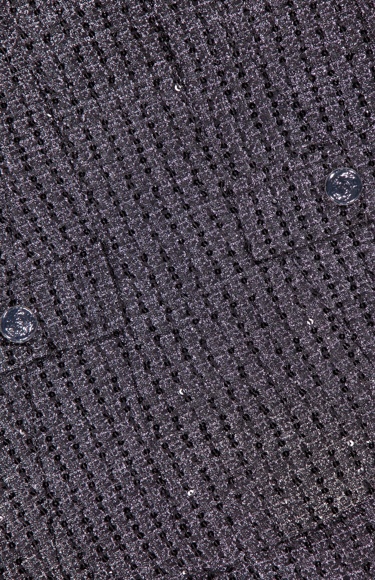 Close-up of the Empire Sparkle Tweed Mini Dress by AMANDA UPRICHARD, featuring textured dark gray fabric with a grid pattern, silver shimmer, and two buttons—ideal for an elegant cocktail look.