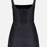 The AMANDA UPRICHARD Rhonda Floral Print Romper is a sleeveless black mini with a square neckline, fitted bodice, smocked center panel, and subtle jacquard floral pattern, displayed on a plain white background.