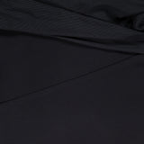 A close-up of the Rosalyn Drape Shoulder Mini Dress by AMANDA UPRICHARD highlights its black fabric, featuring elegant draping, soft diagonal lines, and gentle shadows across the material.