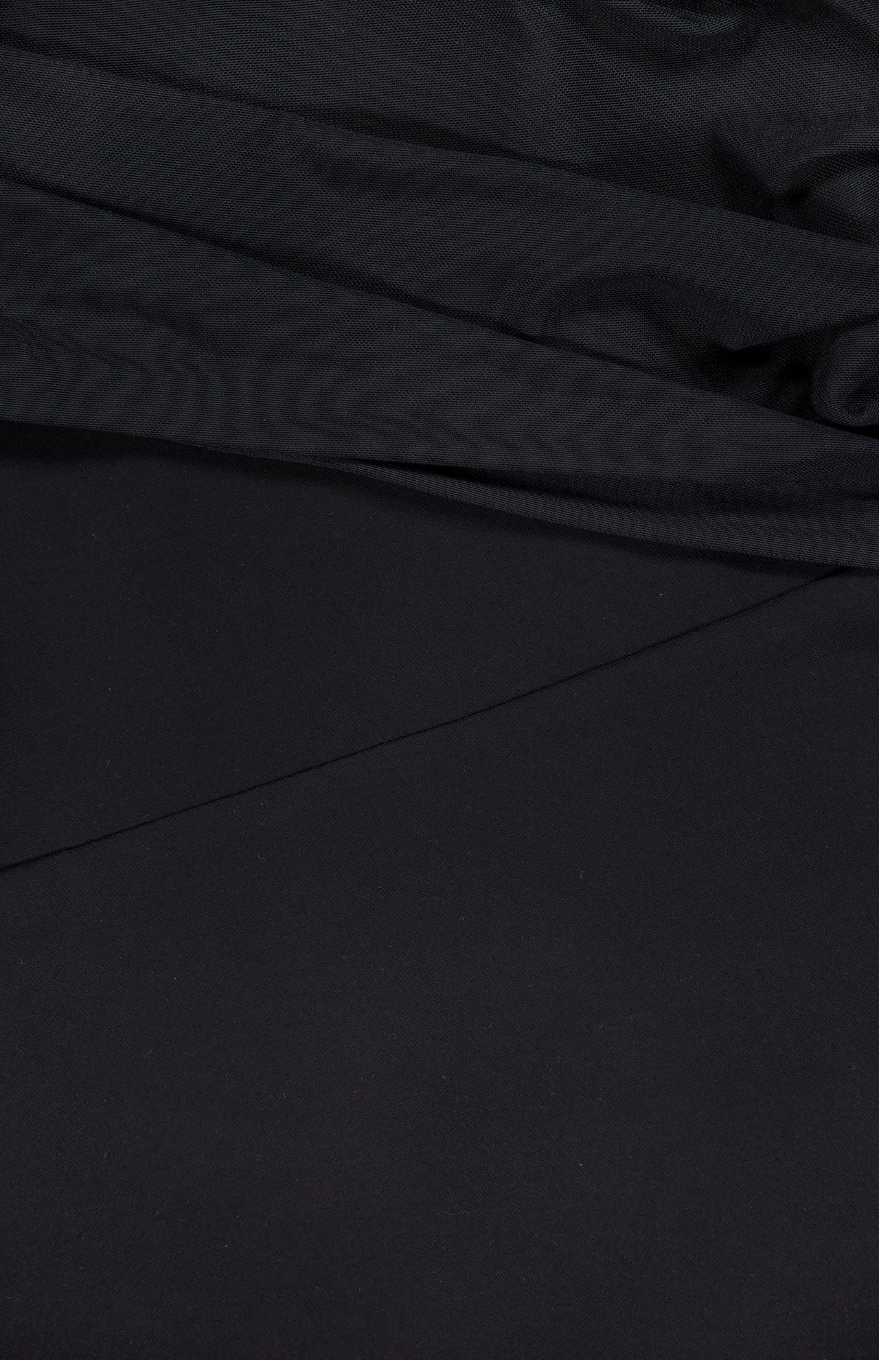 A close-up of the Rosalyn Drape Shoulder Mini Dress by AMANDA UPRICHARD highlights its black fabric, featuring elegant draping, soft diagonal lines, and gentle shadows across the material.