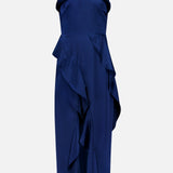 The Alessandra Ruffle Maxi Dress by AMANDA UPRICHARD is a sleeveless navy satin maxi with a halter neckline, cascading side ruffles, and a flowing high-low hem—perfect for special occasions.