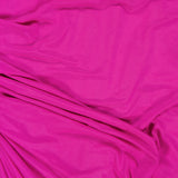 The Brooke Ruched One Shoulder Dress by AMANDA UPRICHARD features bright pink fabric with gentle drapes, creating soft, flowing lines and subtle shadows reminiscent of a chic hot pink dress.