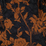 Close-up of the Amanda Uprichard Florencia Maxi Dress with High-low Bubble Hem, a black maxi dress featuring an embossed rose pattern in burnt orange.