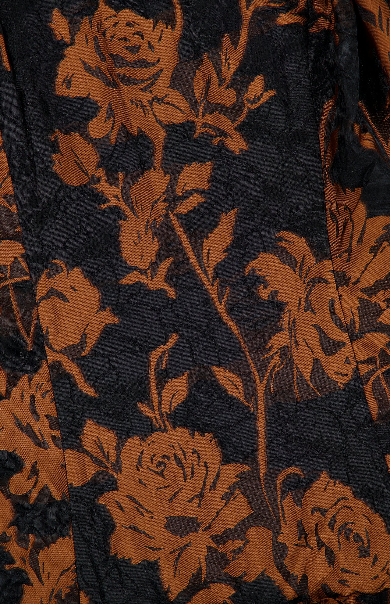 Close-up of the Amanda Uprichard Florencia Maxi Dress with High-low Bubble Hem, a black maxi dress featuring an embossed rose pattern in burnt orange.