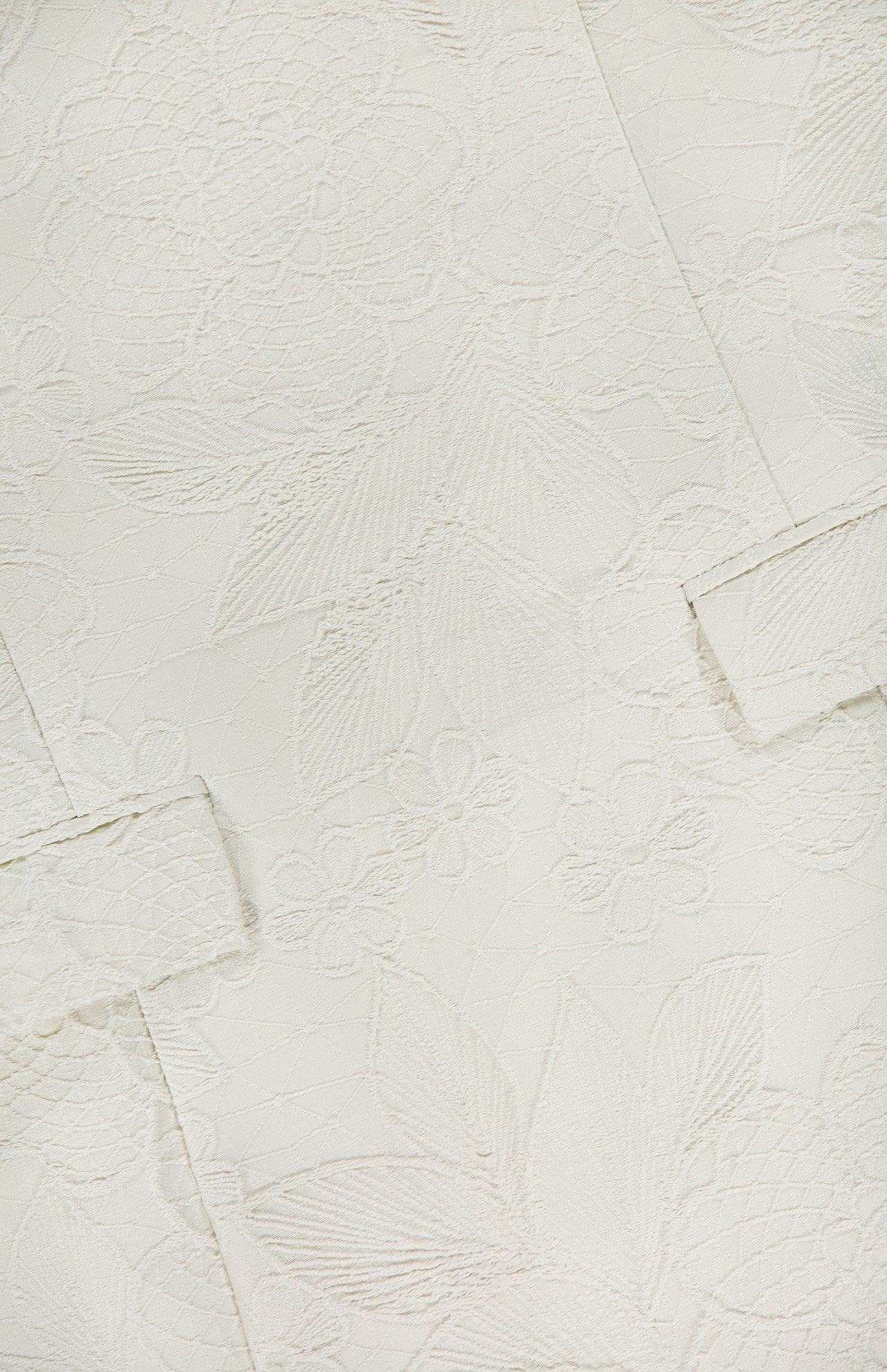 Close-up of the AMANDA UPRICHARD Isabella Fit & Flare Mini Dress, featuring textured off-white fabric with an intricate floral and leaf pattern—overlapping rectangular sections add chic depth, perfect for a bridal shower.