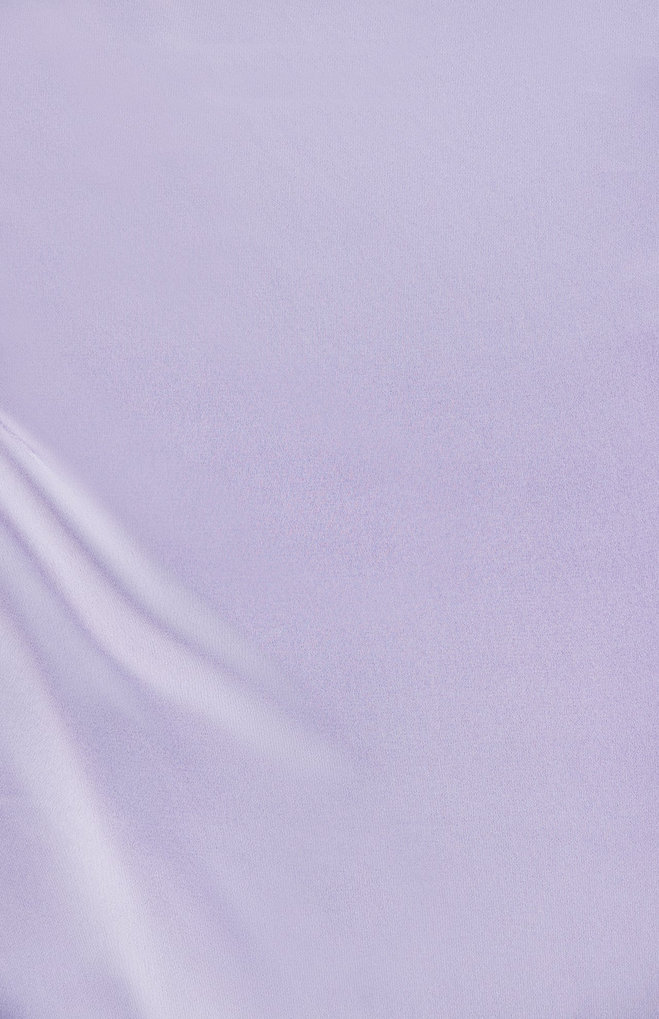 The smooth lavender-colored fabric of the Jean Ruched Knot Midi Dress by AMANDA UPRICHARD features soft folds in the lower left corner, creating gentle lines and a subtle sheen. The overall appearance evokes calm and minimalist cocktail attire, reminiscent of luxurious silk.