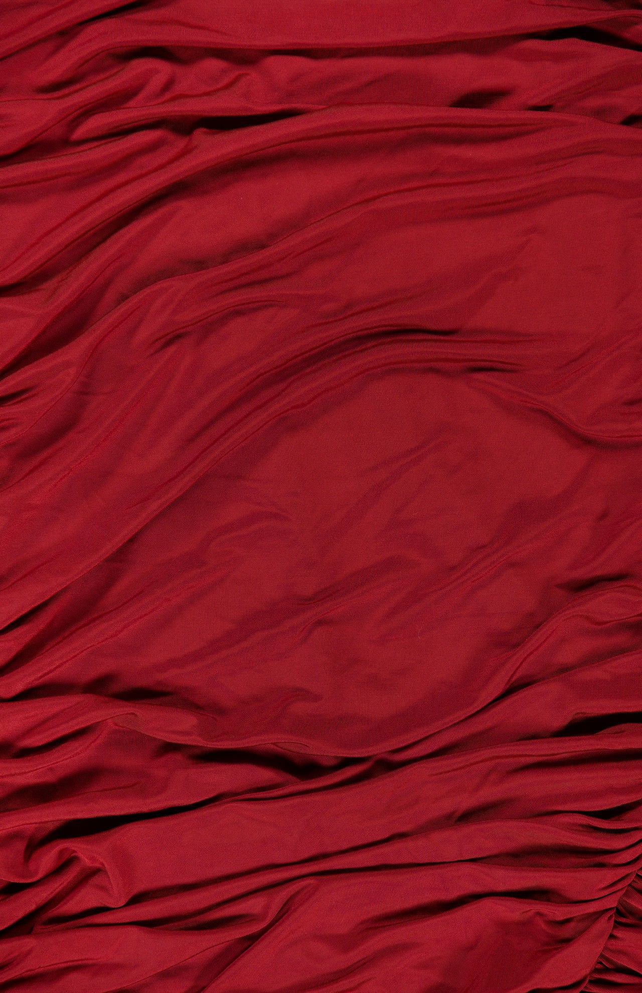 The Katya Draped Panel Mini Dress by AMANDA UPRICHARD features a rich red fabric with soft, wavy folds and ripples that create a textured look reminiscent of gathered ruching. The smooth, slightly glossy material catches the light in certain areas, adding to its elegant and refined appearance.
