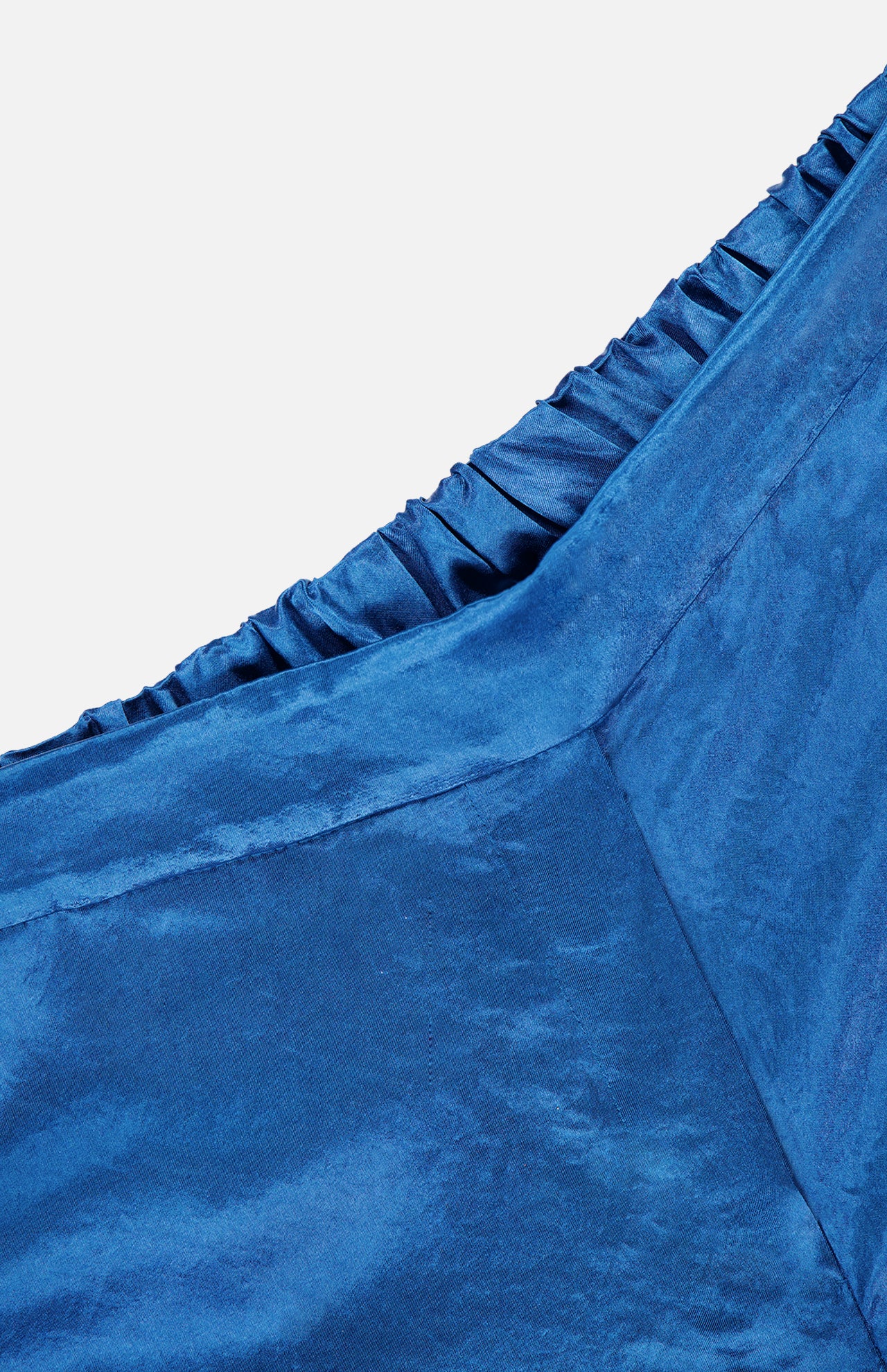 Close-up of blue satin fabric with gathered, ruched detail along the seam, highlighting the smooth, glossy texture of AMANDA UPRICHARD's Kordell Satin Pants—perfect for resort wear or elegant occasions.