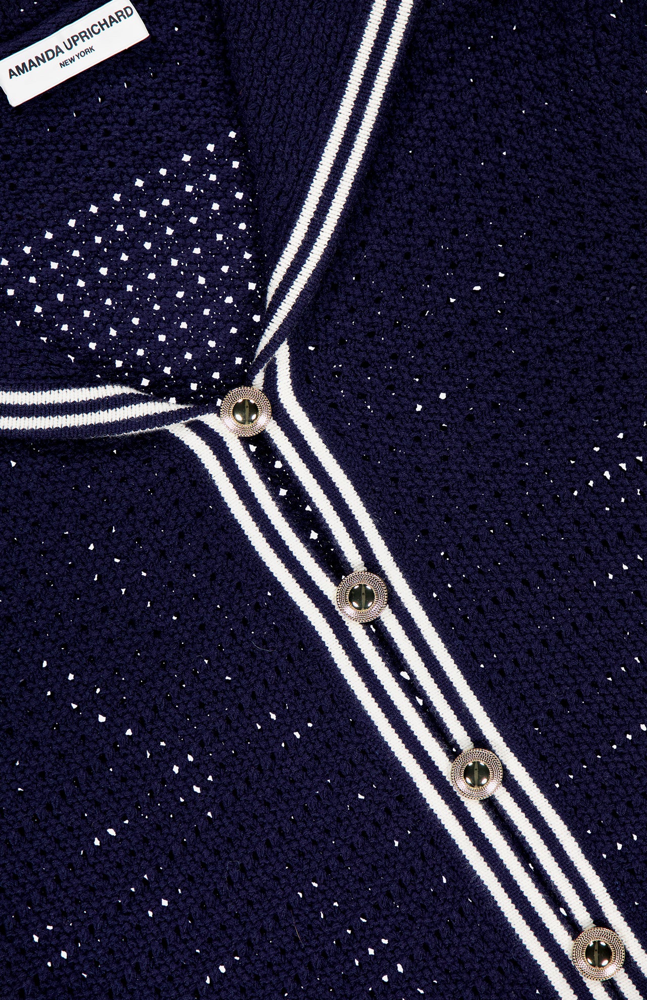 Close-up of the Monique Sailor Neckline Cardigan by AMANDA UPRICHARD, featuring navy knit with white perforated dots, striped placket, four silver buttons, and a brand label for a classic nautical look.