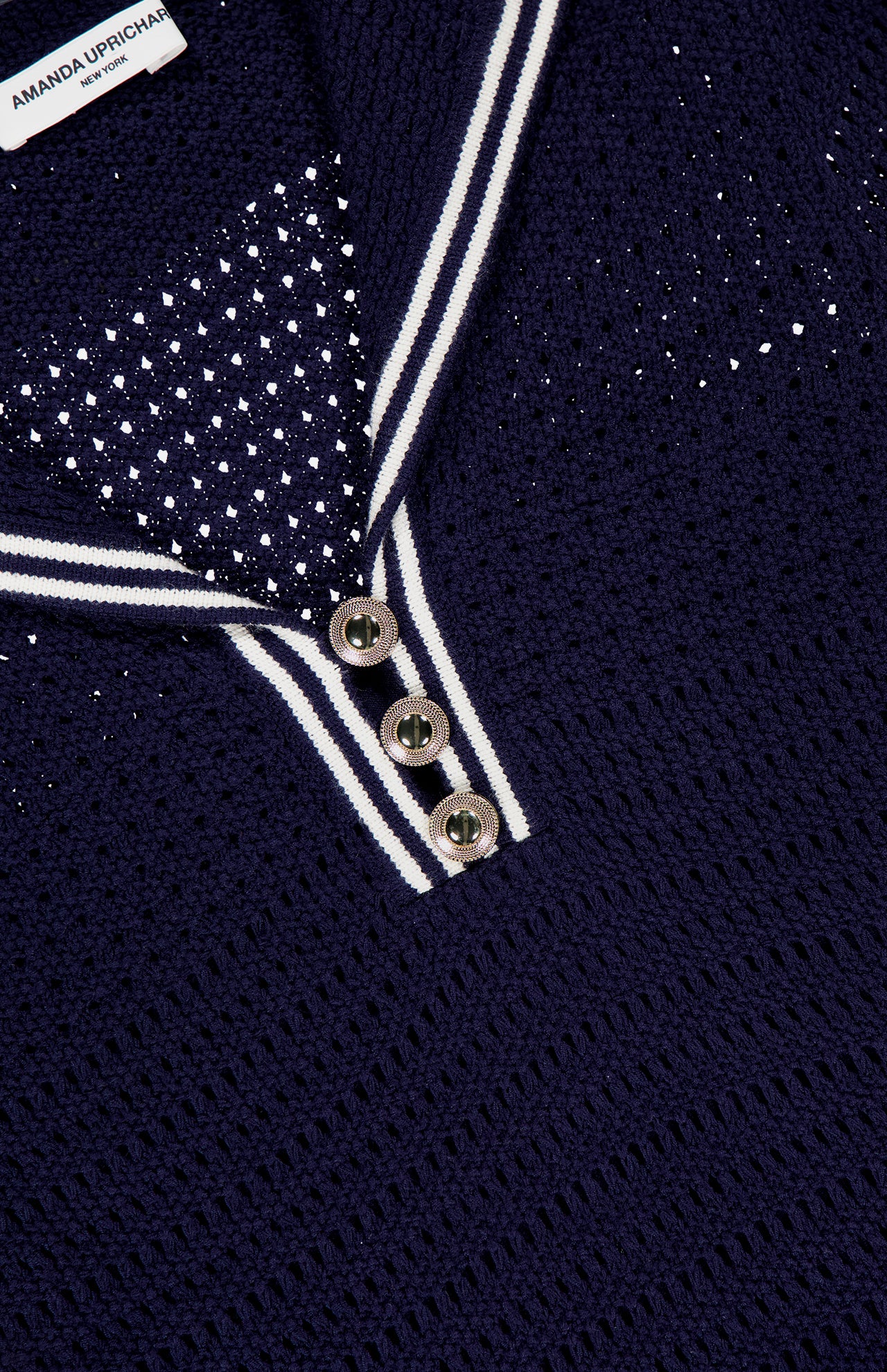 Close-up of the Monique Sailor Neckline Dress by AMANDA UPRICHARD, a navy blue textured knit with a white-striped sailor collar, three silver buttons, scattered small white embellishments, and the AMANDA UPRICHARD label.