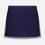 The Monique Knit Mini Skort by AMANDA UPRICHARD features a navy blue crochet design, fitted silhouette, and white trim on the hem and sides, offering both elegance and comfort. Displayed against a plain white background.