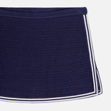 A close-up of the Monique Knit Mini Skort by AMANDA UPRICHARD, featuring a fitted navy silhouette with mesh texture and white double stripes along the hem, displayed on a white background.